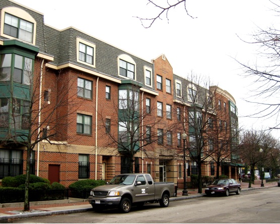A row of brick buildings with cars parked on the side.
