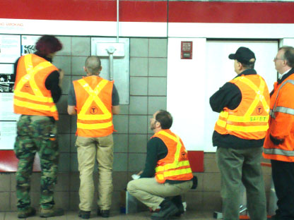A group of people in safety vests are standing by the wall.